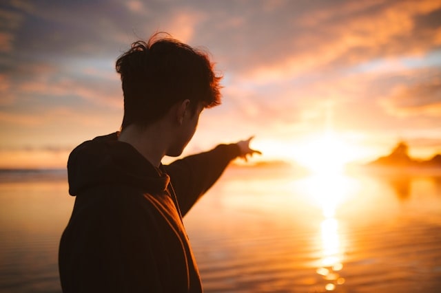 夕日に向かって指を指し決意表明する男性の実写画像