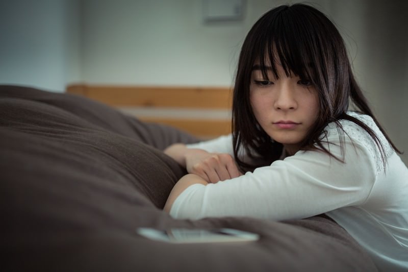 ベッドでスマホを見つめる女性の実写画像